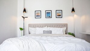 Un lit bien fait, avec une couette blanche, une tête de lit capitonnée et trois tableaux encadrés accrochés au mur.
