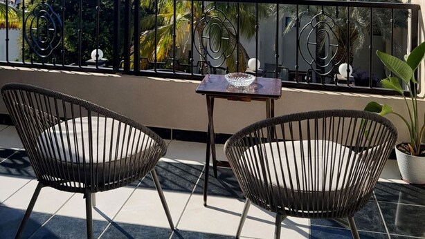 Un balcon avec deux chaises, une petite table et un pot de fleurs.