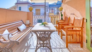 A balcony with a wooden bench, a table with a vase of flowers, and wooden chairs. - VFH Blue Breeze Holiday Home (Porticello)