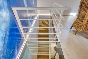 Una escalera moderna con barandillas de vidrio y peldaños de madera que conduce a un nivel superior.