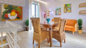 A dining area with wicker chairs, a wooden table, and a painting of fruit on the wall. - VFH Blue Breeze Holiday Home (Porticello)