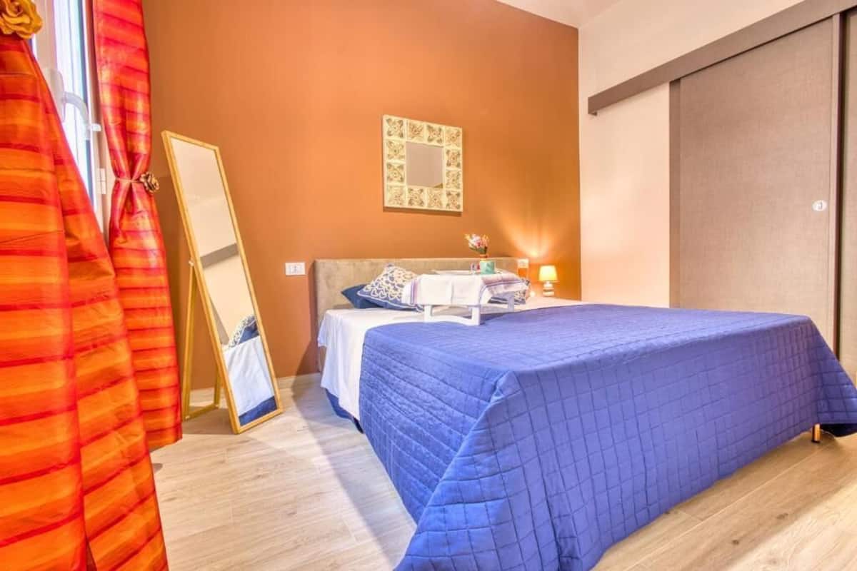 A bedroom with a bed, a bedside table, a mirror, and a wall-mounted artwork.