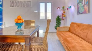 A modern living room with a glass-top dining table, wicker chairs, a sofa, and a decorative plant. - VFH Blue Breeze Holiday Home (Porticello)
