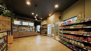 A grocery store interior with wooden shelves, refrigerated sections, and a checkout counter. - Student Only West End (Glasgow)