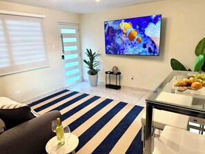 A living room with a striped rug, a TV mounted on the wall, a glass coffee table, and a plant. - Luxe Black & White Apt I (Trujillo Bajo)