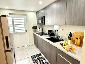 A modern kitchen with grey cabinets, a black sink, and a countertop with fruits and a coffee maker. - Luxe Black & White Apt I (Trujillo Bajo)