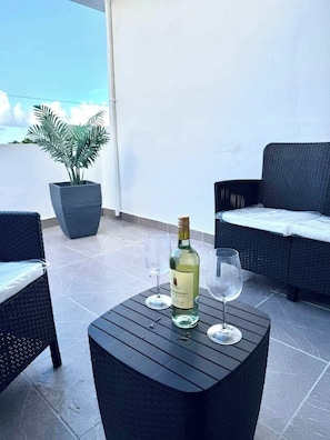 A patio area with two wicker chairs, a small round table, a bottle of wine, and a glass on the table. - Luxe Black & White Apt I (Trujillo Bajo)