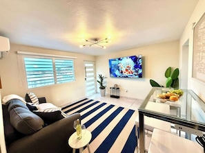A modern living room with a sofa, a glass coffee table, a striped rug, a flat-screen TV, and a small table with snacks. - Luxe Black & White Apt I (Trujillo Bajo)