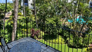 A balcony with a tiled floor, surrounded by lush greenery and palm trees, overlooking a pool area. - Puerto de Luna: Double Room with Kitchen & Pool Access (Puerto Vallarta)