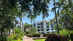 A pathway leading to a building with multiple balconies, surrounded by lush greenery and palm trees. - Puerto de Luna: Double Room with Kitchen & Pool Access (Puerto Vallarta)