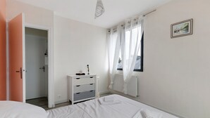 A bedroom with a bed, a bedside table, a radiator, and a window with curtains.