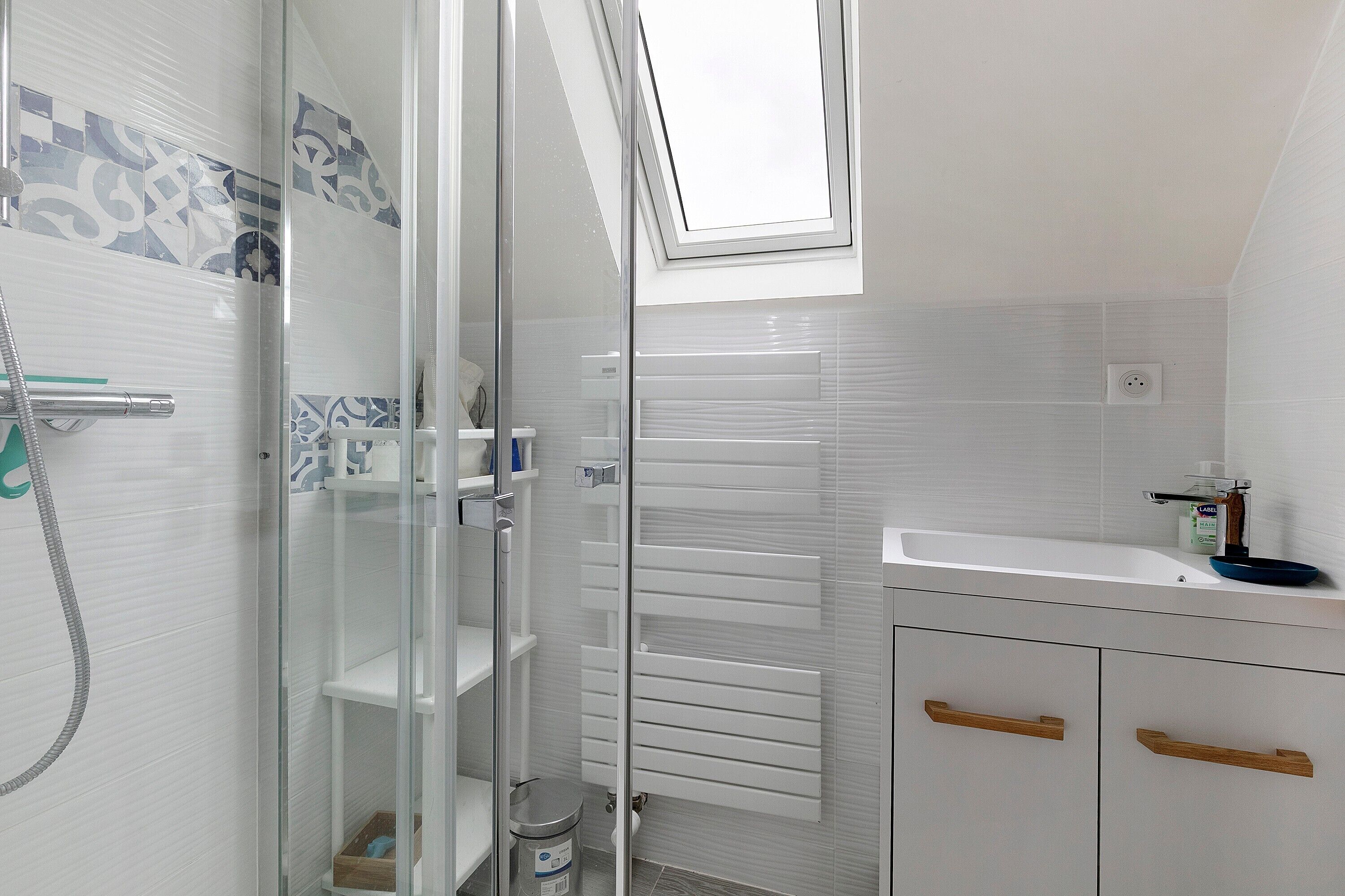 Une salle de bain moderne avec une douche à parois de verre, un lavabo blanc et un radiateur encastré.