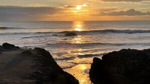 A sunset over the ocean with waves and rocky foreground.