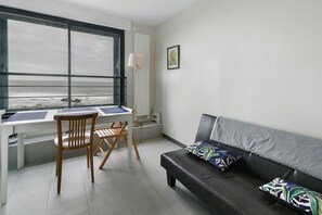 Una habitación con escritorio, silla, sofá, lámpara y ventana con vista al mar.