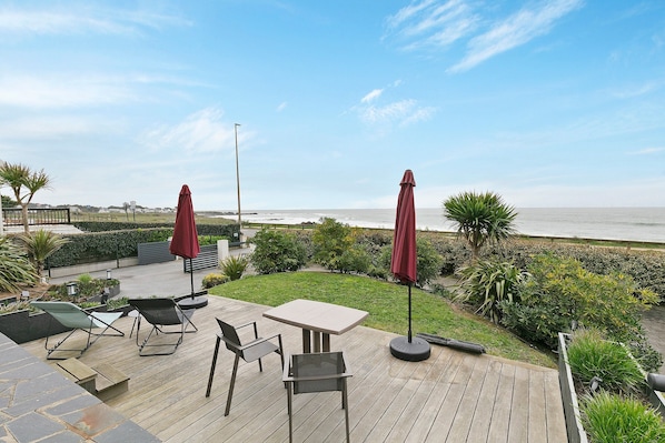 Una terraza de madera con mobiliario exterior, una mesa y dos sombrillas.