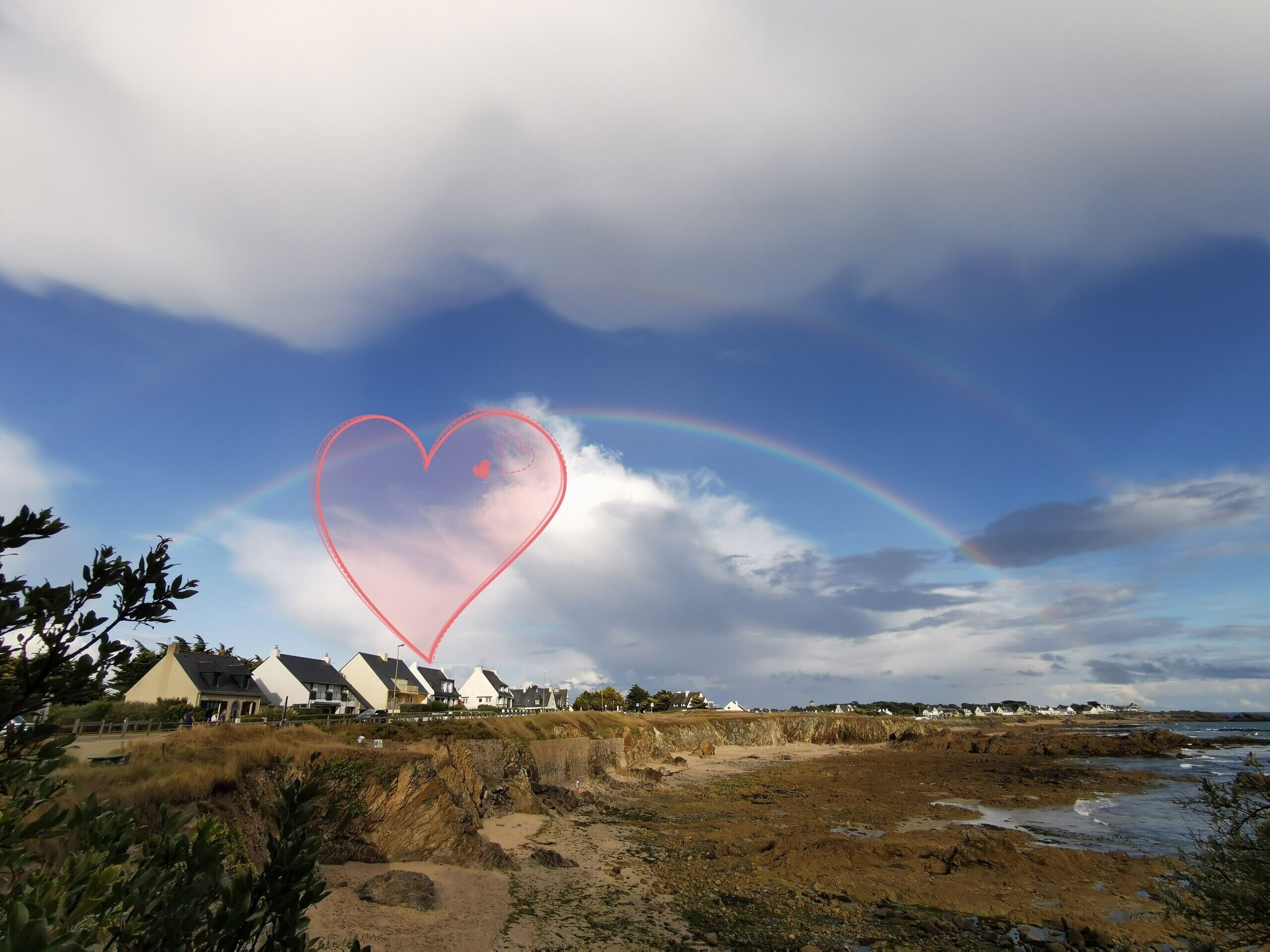 A coastal landscape with houses, a beach, and a rainbow.