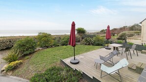 Eine Terrasse mit Gartenmöbeln und Sonnenschirmen mit Blick auf einen angelegten Garten und den Ozean.