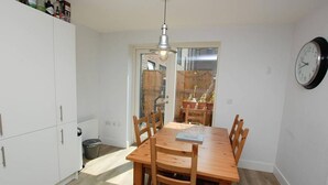 A dining area with a wooden table and chairs, a white cabinet, a clock, and a window with a view of the outside. - Room-ensuite Double Bed Room Sunny Spaci (Nottingham)