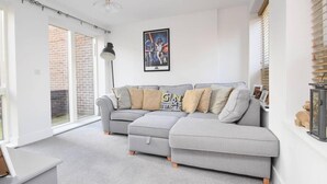 A modern living room with a grey sectional sofa, a framed poster on the wall, and a large window with blinds. - Room-ensuite Double Bed Room Sunny Spaci (Nottingham)