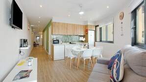 Ein modernes Wohnzimmer mit einer Couch, einem Esstisch mit Stühlen, einer Küchenzeile mit Mikrowelle und einem an der Wand befestigten Fernseher.