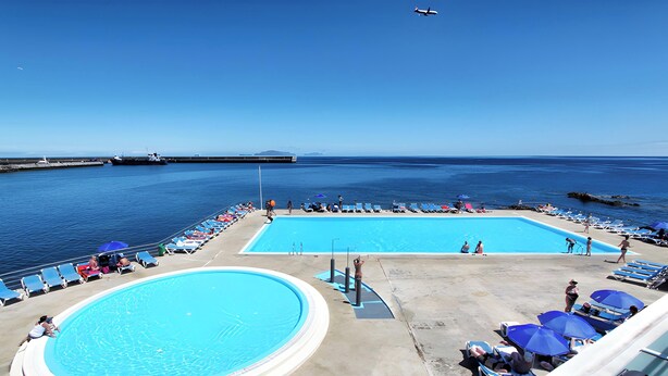 Ein Poolbereich mit Liegestühlen und Sonnenschirmen, ein großes Schwimmbecken und Meerblick.