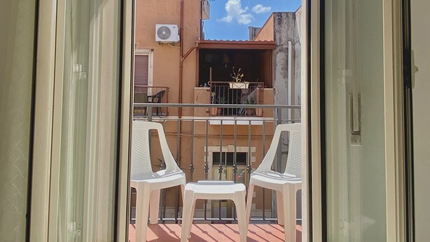 Un balcón con una mesa y sillas, vistas de un edificio y cielo despejado.