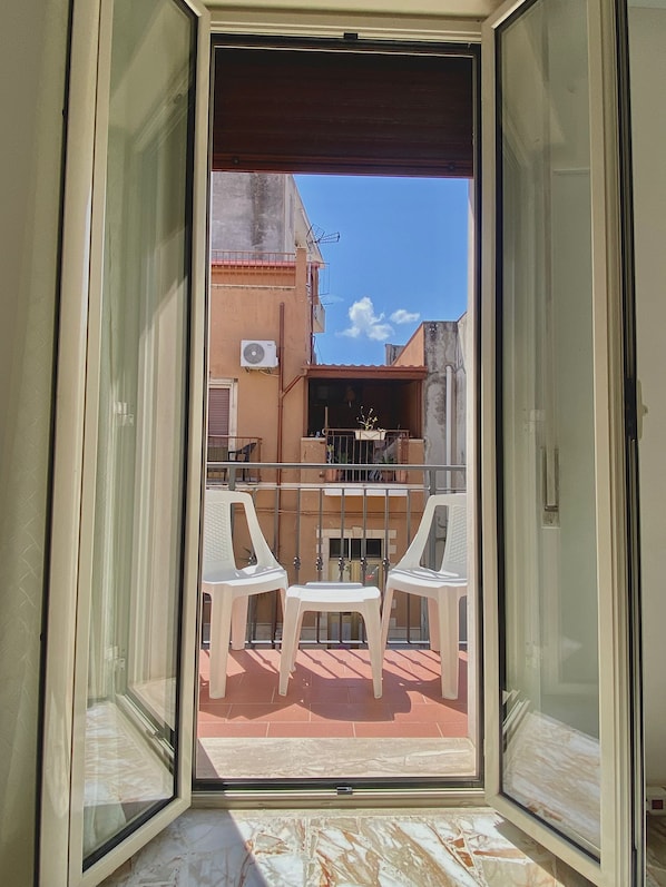 Un balcón con una mesa y sillas, vistas de un edificio y cielo despejado.