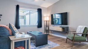 A modern living room with a flat-screen TV mounted on the wall, a ceiling fan, a sofa, a coffee table, and a chair. - Cozy townhouse with community pool, heart of Tempe near ASU (Tempe)