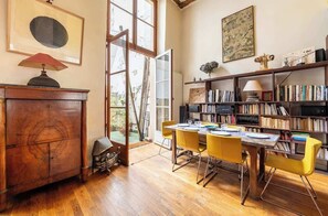 A room with a wooden cabinet, a bookshelf, a dining table with yellow chairs, and a large window.