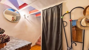 Een kamer met een marmeren aanrecht, een zwart gordijn, een spiegel, een hoedenrek en een trap.