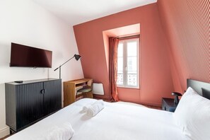 A bedroom with a bed, a TV, a desk, a chair, and a window with curtains. - Central Apartment – Near the Champs-Élysées (Paris)