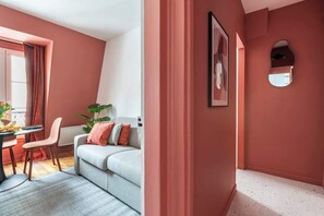 Ein modernes Wohnzimmer mit einem grauen Sofa, einem Esstisch mit Stühlen und einem großen Fenster mit Vorhängen.
