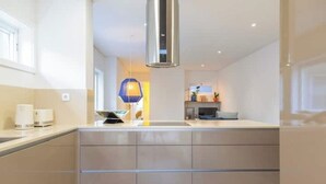 Una cocina moderna con una isla central, campana extractora de acero inoxidable y una lámpara colgante.