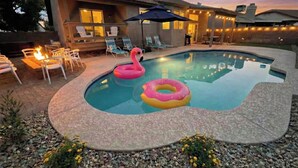 En swimmingpool med to lyserøde flamingo-flydere, omgivet af liggestole og et bålsted.