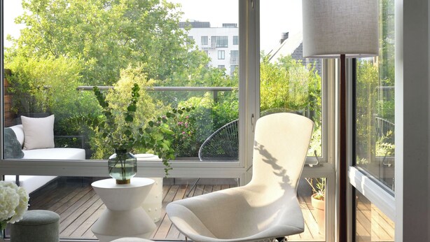 A modern living room with large windows, a white chair, a floor lamp, and a coffee table.