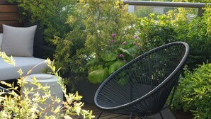 A wooden deck with a black wire chair, a white sofa, and various potted plants.