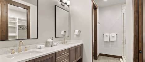 A modern bathroom with two sinks, a large mirror, and a shower area.