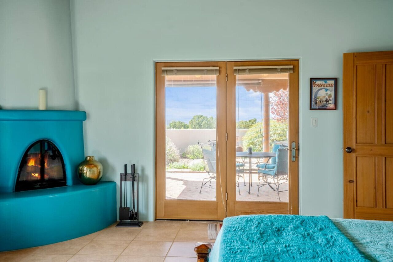 Une pièce avec un canapé de couleur turquoise, une cheminée, une porte-fenêtre coulissante donnant sur une terrasse extérieure avec une table et des chaises, et une porte en bois.
