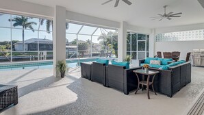 Un'ampia area interna con vista piscina, arredi in vimini, ventilatori a soffitto e un'ampia finestra.