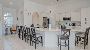 Una cucina moderna con mobili bianchi, un'isola centrale con sgabelli da bar e una zona pranzo con sedie.