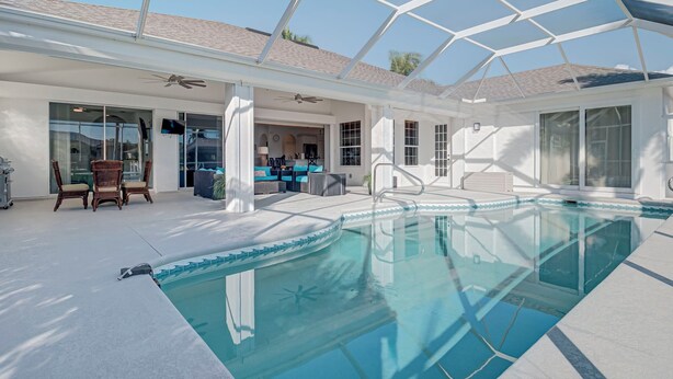 Area piscina interna moderna con pareti vetrate, ventilatori a soffitto e zona relax con mobili in vimini.