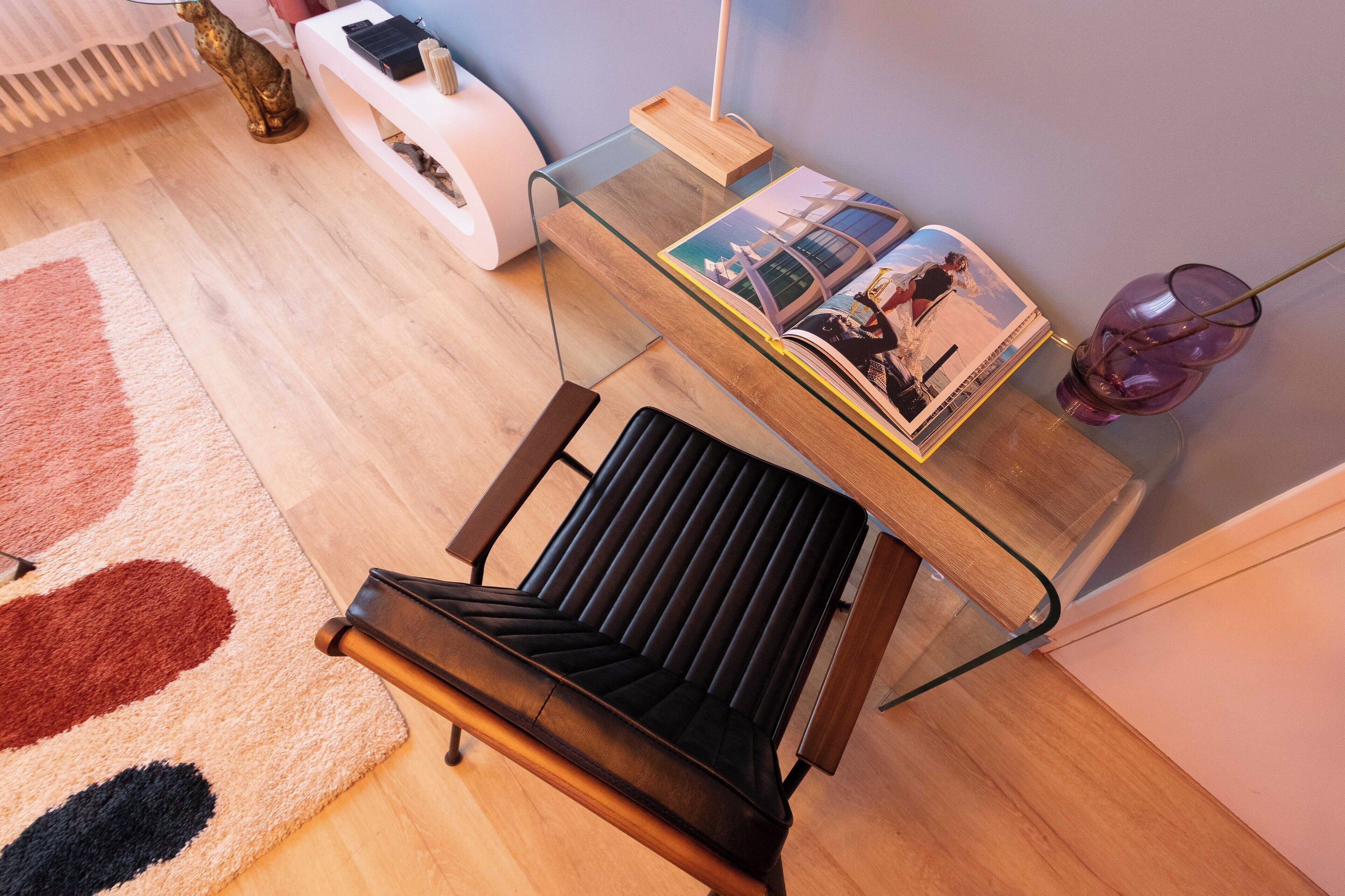 Ein modernes Wohnzimmer mit einem Glastisch, einem schwarzen Sofa, einem Holztisch und einer Zeitschrift.