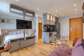 A modern hotel room with a bed, desk, kitchenette, and a seating area with chairs. - Moderno Studio nos Jardins Funcional e com Lazer (São Paulo)