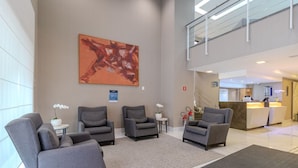 Un hall d’entrée avec des fauteuils gris, un grand tableau abstrait, un comptoir d’accueil et un escalier.