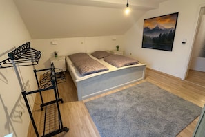 A bedroom with a bed, a grey rug, a coat rack, and a painting on the wall.