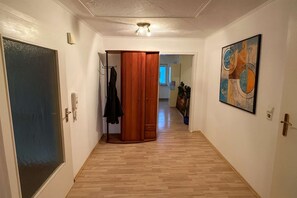 A hallway with wooden flooring, a coat rack, a door, and a painting on the wall. - Tor zu Frankreich – modern apartment in a unique location (Neuburg am Rhein)