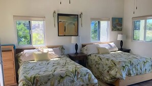 A room with two beds, each with a floral bedspread, a painting on the wall, and a window with a view of greenery. - Escape Casita – Incredible Ocean Views, A/C & Heated Saltwater Pool (Todos Santos)