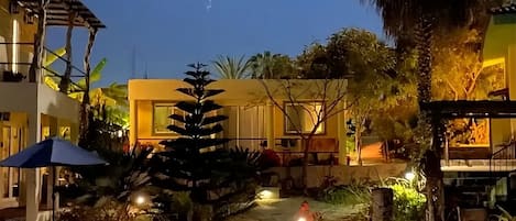A well-lit outdoor area with a pool, palm trees, and a building with a yellow facade.