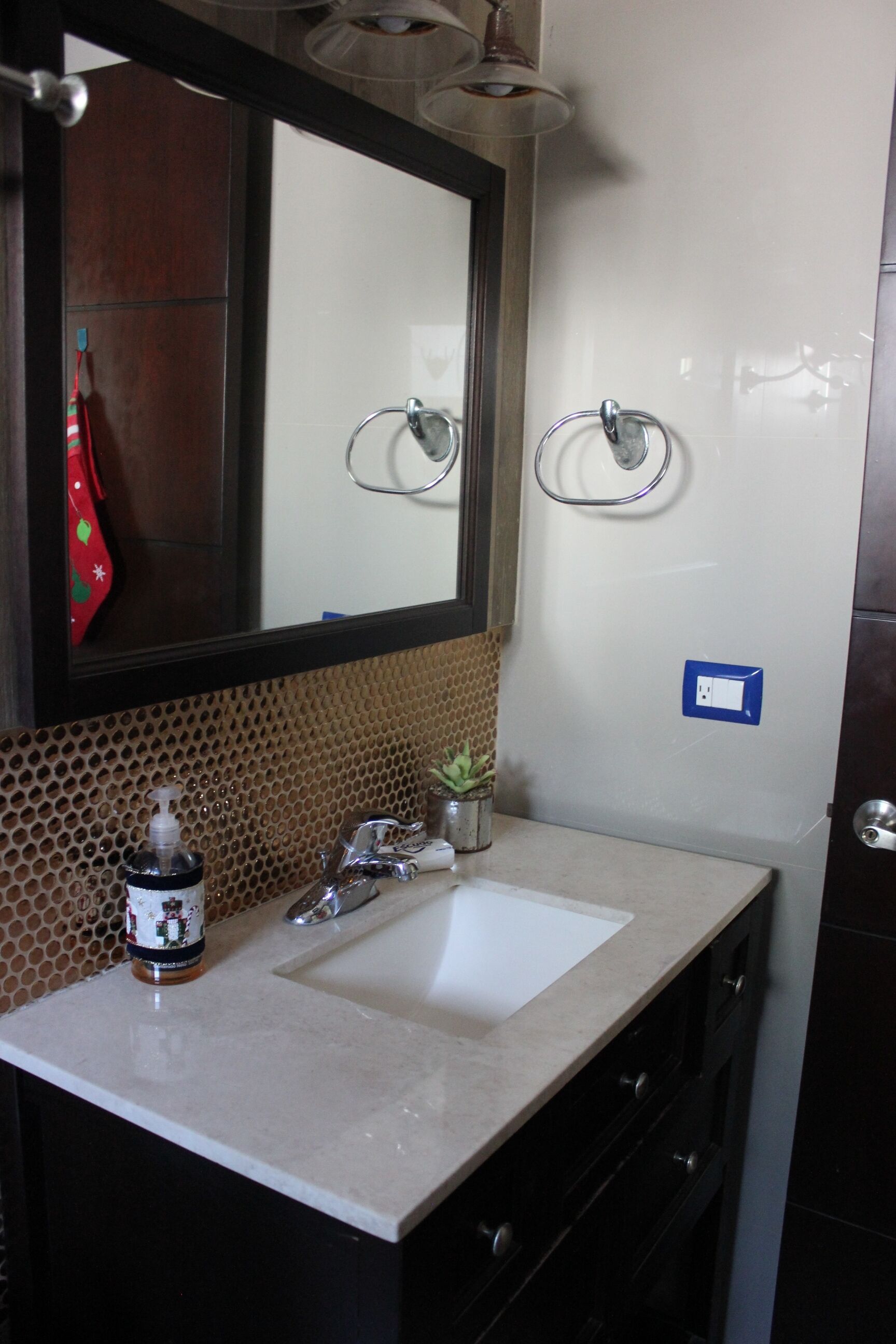 Un bagno con lavandino, specchio, porta asciugamani e una pianta in vaso.