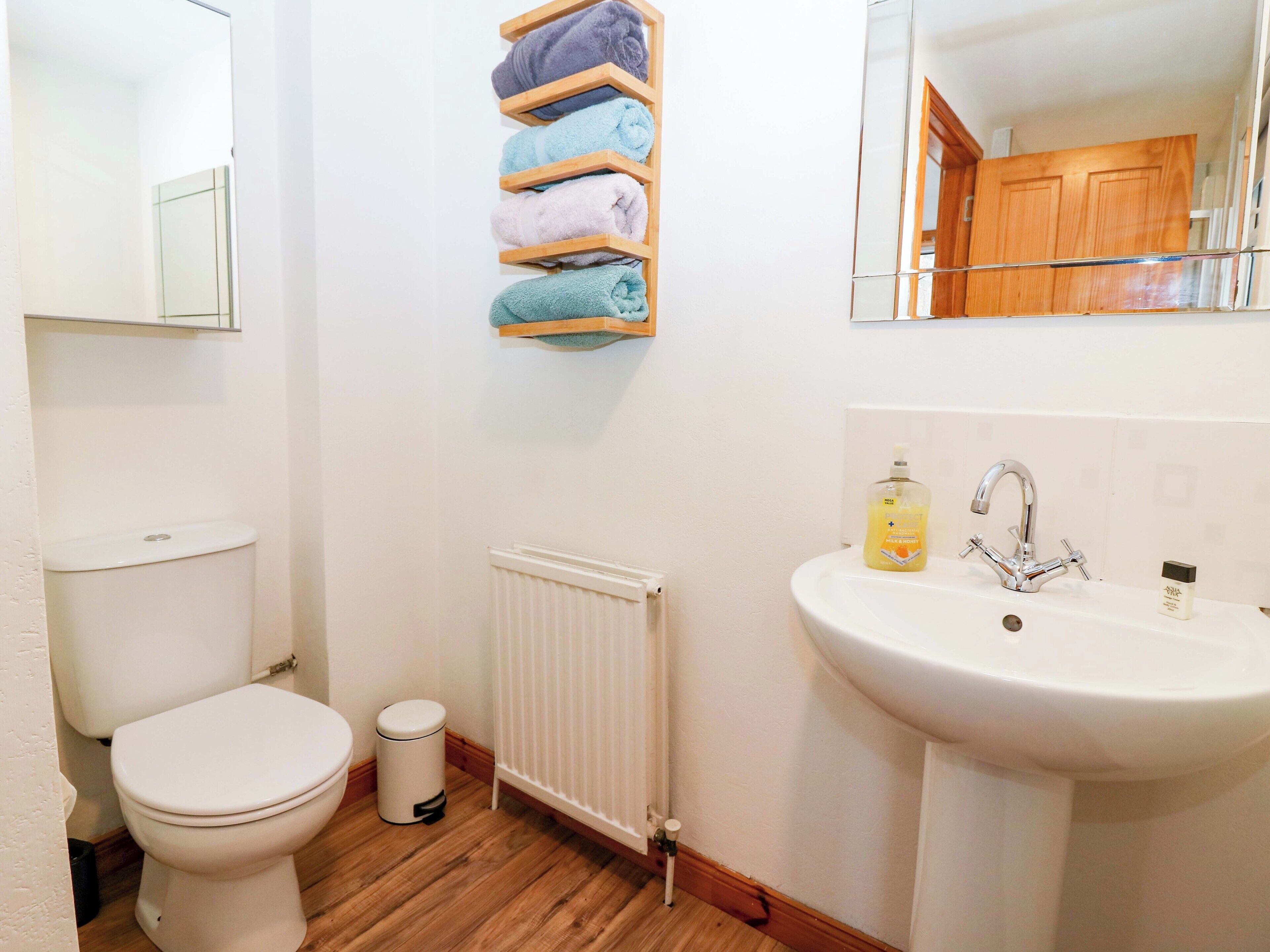 Une salle de bain comprenant des toilettes, un lavabo, un radiateur et une étagère avec des serviettes pliées.